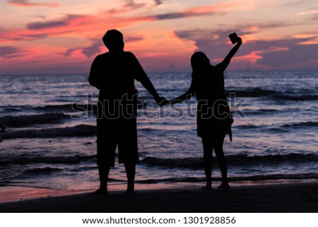 The black silhouette, the couple standing hand in hand by the sea in the evening atmosphere at sunset.