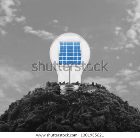 Light bulb with solar cell inside on pile of soil over black and white sky, Ecological power and energy concept