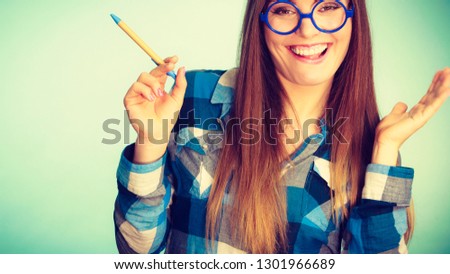 Studying, education and fun concept. Happy smiling nerdy thinking woman in weird big glasses having idea and holding pen. Studio shot on blue background