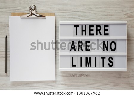 Lightbox with text 'There are no limits', clipboard with sheet of paper and pencil on a white wooden table, top view. Flat lay, overhead.