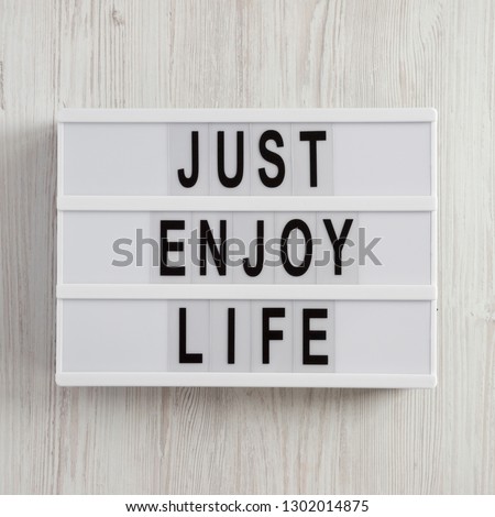 Modern board with text 'Just enjoy life' on a white wooden surface, top view. Overhead, from above.