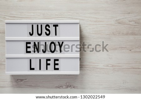 Modern board with text 'Just enjoy life' on a white wooden background, top view. Copy space.