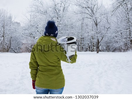 Woman with white ice skates looks at the snow-covered garden
