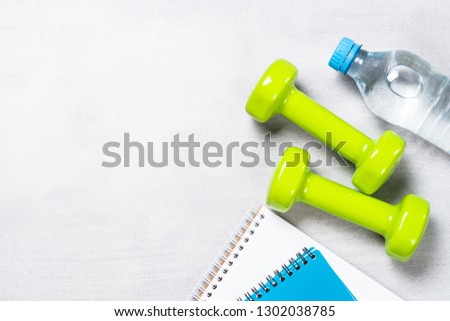 Dumbbells, notepad, water and apple on light stone background top view with copy space. Fitness concept and healthy lifestyle.