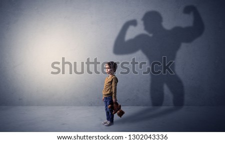 Little waggish boy in an empty room with musclemen shadow behind