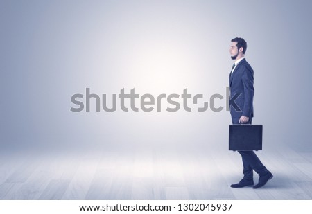 Successful businessman walking in front of an empty wall with briefcase on his hand
