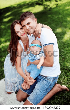 Happy family. Smiling parents with cute child. Handsome father and young mother holding little daughter and having fun in the park. Beautiful woman and strong man sitting on the grass with baby.