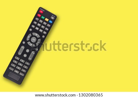 Single black plastic remote control for different multimedia devices on yellow background with copy space for your text. Top view