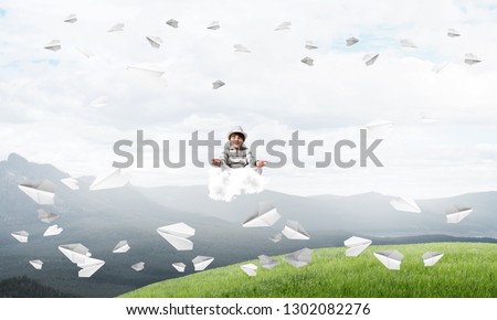 Young little boy keeping eyes closed and looking concentrated while meditating on cloud in the air with beautiful and breathtaking landscape on background.