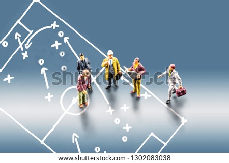 group of miniature business men figurines standing together and leading a discussion with the picture of soccer footbal field with play tactics and strategy drawn on blue background