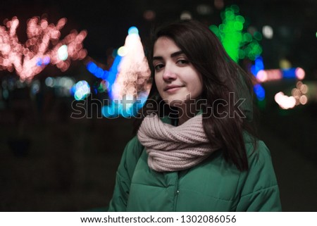 Young cute woman standing on the winter decorated street. Bright bokeh lights on background. Holidays mood.