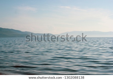 Summer day marine landscape with wavy sea and mountains in a fog. Atmospheric chill foggy picture, concept of tranquility, mystery, calm water of lake Baikal