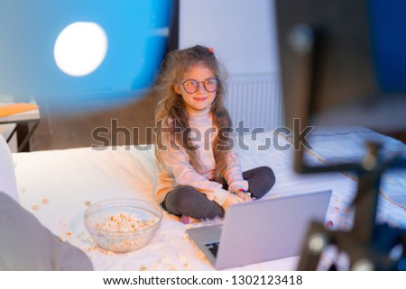 Pretty kid. Cute long-haired girl wearing big eyeglasses looking relaxed while sitting on a bed