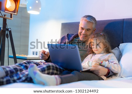 Cartoon time. Grey-haired father and his small pretty daughter feeling good while watching video in a laptop