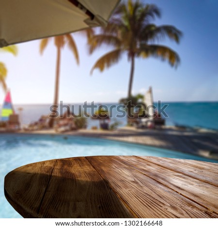 Wooden table of free space for your decoration and exotic landscape of sea palms and blue water. Sunset time. 