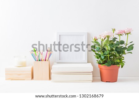 Home interior with decor elements. White frame, pink roses in a pot, interior decoration