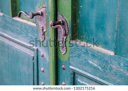 Metal, handmade door handle on green painted wooden door close up shot.