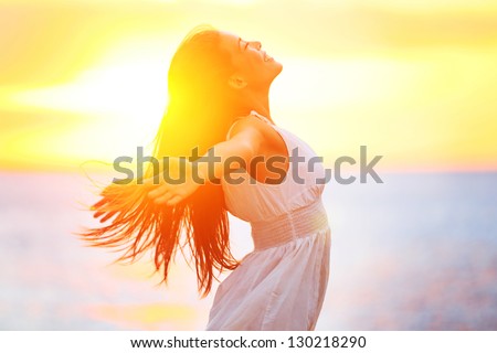 Enjoyment - free happy woman enjoying sunset. Beautiful woman in white dress embracing the golden sunshine glow of sunset with arms outspread and face raised in sky enjoying peace, serenity in nature Royalty-Free Stock Photo #130218290