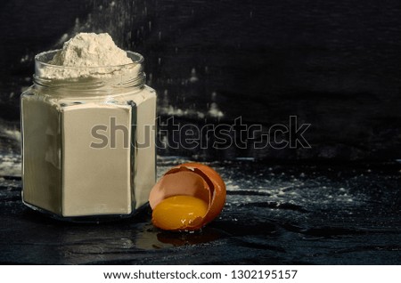 Flour in a jar with a broken egg on a dark background.