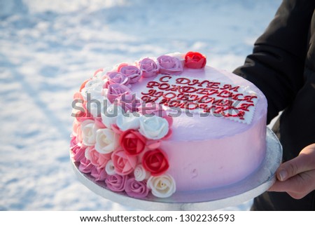 Beautiful cake with pink flowers in the hands of a girl on a background of snow. The inscription on the cake, translated from Russian: Happy Birthday, my dear mommy!