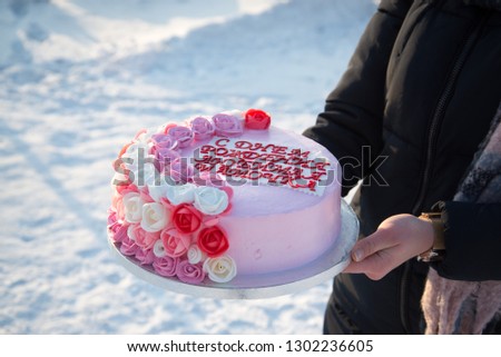 Beautiful cake with pink flowers in the hands of a girl on a background of snow. The inscription on the cake, translated from Russian: Happy Birthday, my dear mommy!
