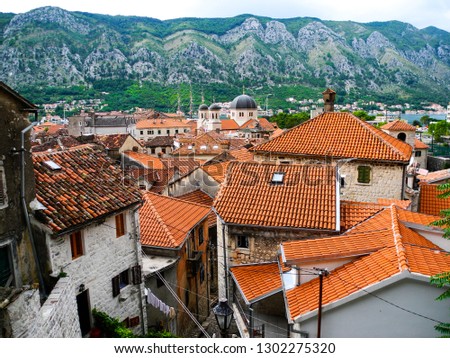 Kotor panoramic view, traditional building with tile roofs and old church. Mountains background. Beautiful rainy summer day.                              