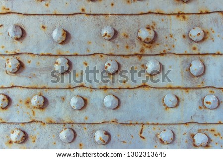 Surface of old metal door with iron rusted texture. Grunge textured metal surface. Rusted grey metal background with orange stains. Row of plates with round rivets as metal pattern.