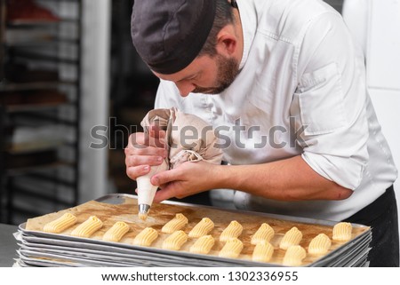 Pastry Chef with confectionary bag squeezing cream at pastry shop . Royalty-Free Stock Photo #1302336955