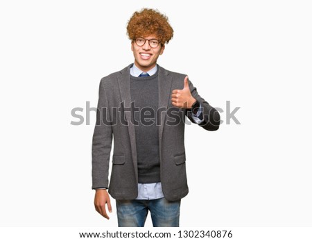 Young handsome business man with afro wearing glasses doing happy thumbs up gesture with hand. Approving expression looking at the camera with showing success.