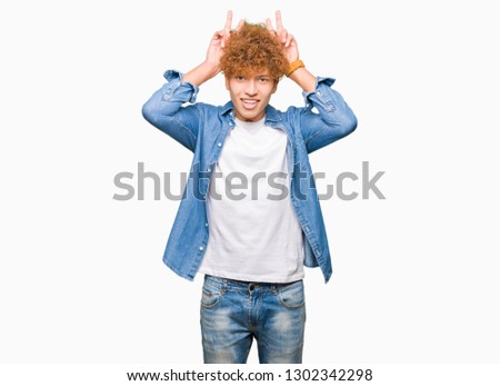 Young handsome man with afro hair wearing denim jacket Posing funny and crazy with fingers on head as bunny ears, smiling cheerful