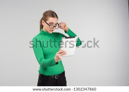 Girl in glasses standing surprised in profile looks on a tablet standing. - Image