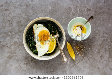 Vegetarian lunch bowl flat-lay. Breakfast with fried egg, kale and sesame seed over grey background, top view. Healthy diet food concept - Image