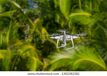 Drone in flight, green trees in the background, selective focus on the drone. 