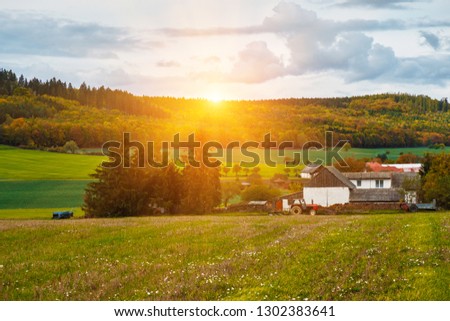 Bright rural landscape with country houses and tractor in the morning sun.