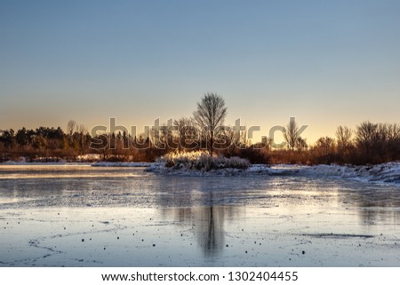 Panoramic Canadian winter landscape near Toronto, beautiful frozen Ontario lake at sunset. Scenery with winter trees, water and blue sky.
