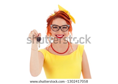 Young Happy Woman holding giving a Car or House Key on White Background. Caucasian person in yellow dress and coral necklace with red lipstick, redhead hair isolated on white studio background Royalty-Free Stock Photo #1302417058
