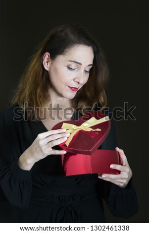 Portrait of a mature woman in her 40s, opening a present box, looking expectantly, thoughtful.