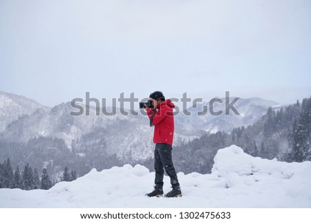 Men wearing red shirts are taking pictures on the mountain while the snow is falling                           