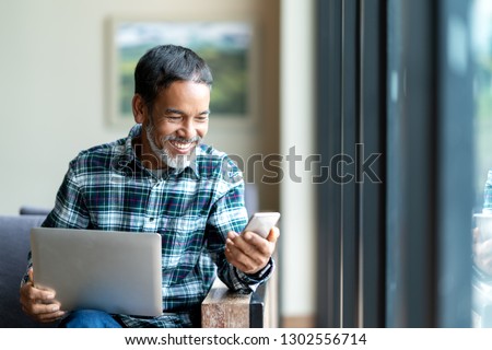 Candid of old asian retired man using mobile phone to transfer money online or financial payment and read text, smile or laugh with happy and positive. Senior asian with digital technology concept. Royalty-Free Stock Photo #1302556714