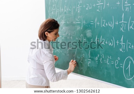 Female math teacher in front of the chalkboard  Royalty-Free Stock Photo #1302562612