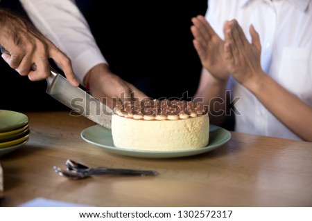 Close up of employee throwing birthday party in office, sitting at table cutting cream pie with knife, excited colleagues celebrate birthday or special occasion eating tart, have fun together