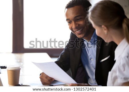 Smiling African American businessman holding female applicant cv, talking with candidate at work interview in office, excited black employer read employee resume at hiring. Recruitment concept Royalty-Free Stock Photo #1302572401