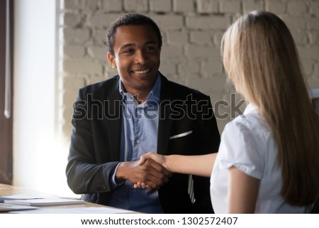 Excited multiracial business partners shake hand congratulate after successful negotiations, happy African American businessman handshake female job applicant greeting at interview. Employment concept