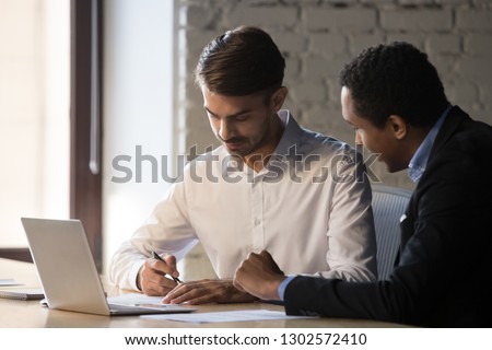 Diverse business partners sign contract after successful negotiations, focused millennial Caucasian businessman put signature on agreement, closing deal with customer. Cooperation concept
