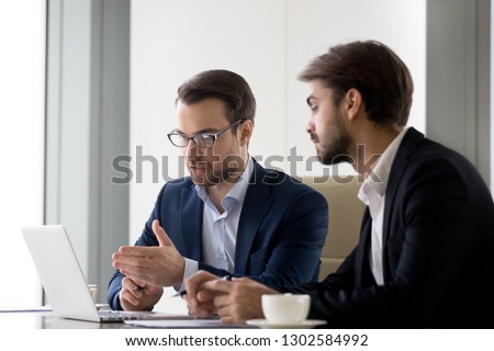 Executive businessmen colleagues working together helping in office teamwork on laptop discuss online project, financial advisor insurer salesman speaking consult client listen computer presentation Royalty-Free Stock Photo #1302584992