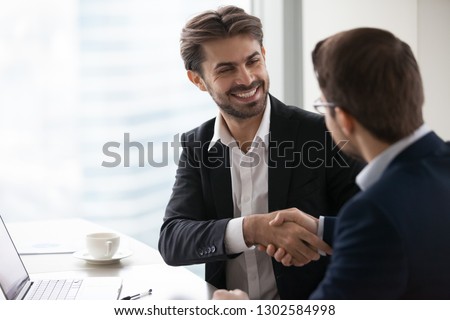 Satisfied happy businessman in suit handshake business partner making deal thanking for teamwork, executive manager and client shake hands after successful negotiations, hiring, forming partnership Royalty-Free Stock Photo #1302584998