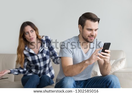 Jealous suspicious mad wife arguing with obsessed husband holding phone texting cheating on cellphone, distrustful girlfriend annoyed with boyfriend mobile addiction, distrust social media dependence Royalty-Free Stock Photo #1302585016
