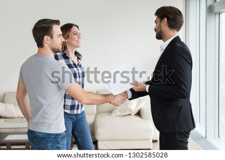 Realtor or landlord handshaking couple buyers tenants make real estate deal holding rental agreement or sale purchase contract, agent and clients shake hands welcoming renters in new home apartment Royalty-Free Stock Photo #1302585028