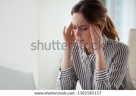 Tired stressed businesswoman feeling strong headache massaging temples exhausted from overwork, fatigued overwhelmed lady executive worker suffering from pain in head or chronic migraine in office Royalty-Free Stock Photo #1302585157