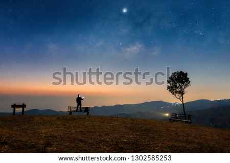 Tourists stand using smartphones on chairs. In the morning, the sky is the Milky Way at Ban Rong Kla Viewpoint, Phitsanulok Province, Thailand.